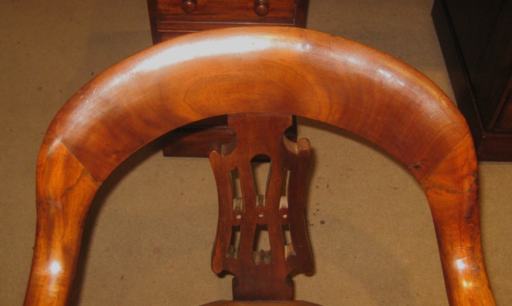 A Victorian walnut revolving desk chair featuring a curved horseshoe backrest, pierced carved splat, circular tan leather upholstered seat with brass studding, and four splayed legs on castors. View III