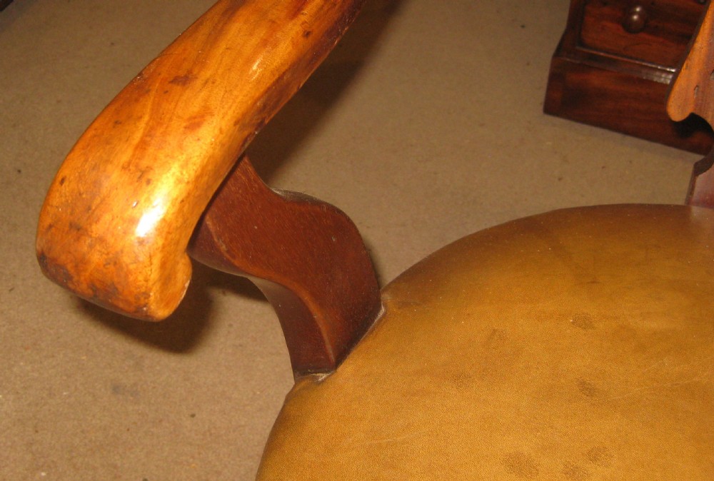 A Victorian walnut revolving desk chair featuring a curved horseshoe backrest, pierced carved splat, circular tan leather upholstered seat with brass studding, and four splayed legs on castors. View V