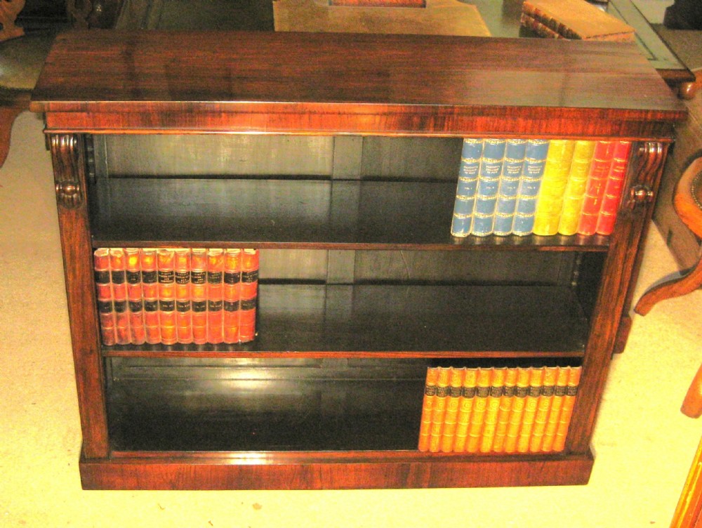 A low Victorian dark rosewood open bookcase with three horizontal shelves, decorative carved side corbels, and a solid plinth base.