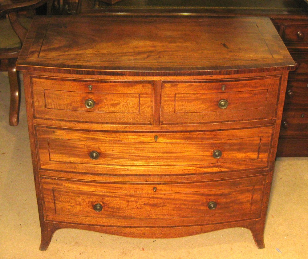 An early Georgian golden mahogany bow-fronted chest of drawers featuring two short drawers over two long drawers with brass knobs and inlaid crossbanding.