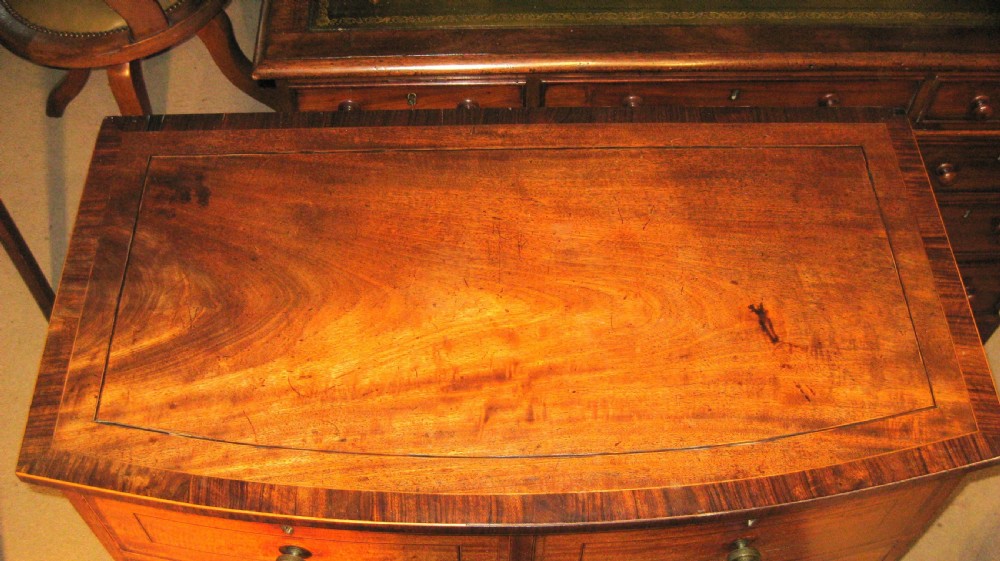 An early Georgian golden mahogany bow-fronted chest of drawers featuring two short drawers over two long drawers with brass knobs and inlaid crossbanding. View IV