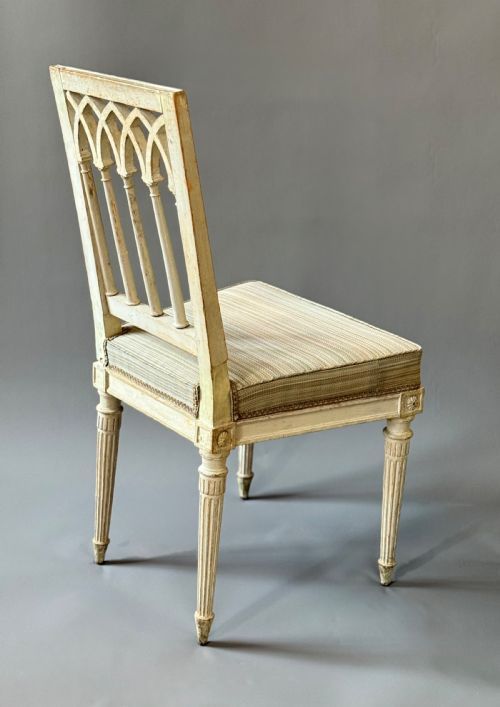 fig 1. A pair of grey painted side chairs featuring openwork gothic arcaded backrests, fluted tapered legs, and striped upholstered seats.