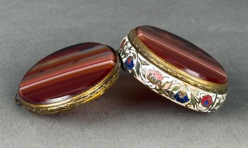 fig 1. An oval nineteenth-century French double-sided box featuring polished banded agate panels on the top and bottom framed by floral white, red, and blue champleve enamel metalwork.