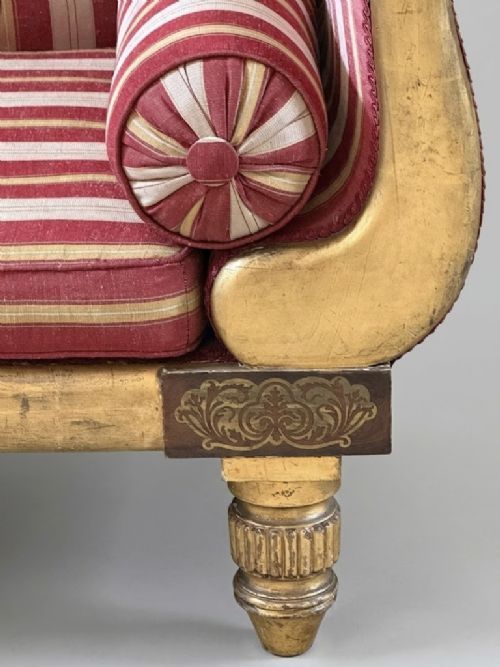 fig 1. A Regency-style giltwood chaise longue featuring scrolled ends, turned legs, red and cream striped silk upholstery, and matching bolster cushions.