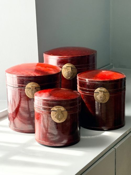 A set of four graduated cylindrical red lacquered wooden boxes featuring brass latch mountings on the front.