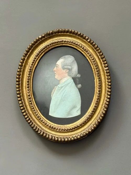 fig 1. A pair of Georgian oval portrait miniatures depicting a profiled lady and gentleman set within beaded giltwood frames against a grey wall.