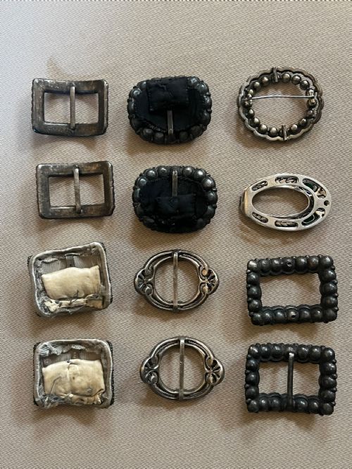 fig 1. A collection of twelve Georgian-era shoe buckles arranged in rows, featuring various oval and rectangular shapes crafted from paste glass, crystal, and cut-steel settings.