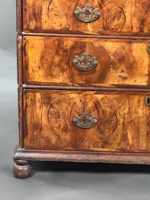 fig 1. An early eighteenth-century Queen Anne chest of drawers in figured walnut veneer featuring a two-over-three drawer configuration and brass drop handles on bun feet.