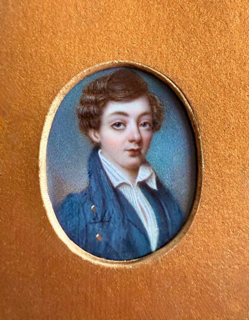 fig 1. An oval 19th-century portrait miniature depicting a young boy with brown hair wearing a blue jacket, set within a gilded frame.