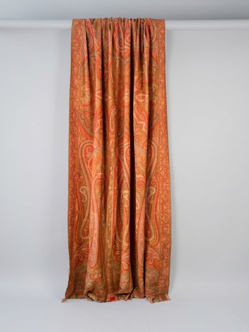 fig 1. A large Victorian woven wool shawl featuring dense teardrop Paisley patterns in shades of terracotta, ochre, and green with a fringed border.
