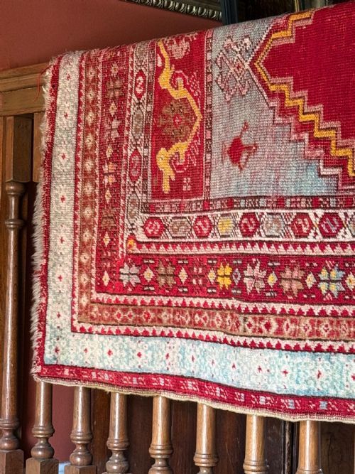 fig 1. A 19th-century hand-knotted Anatolian prayer rug featuring a central red field with a stepped arch motif, framed by decorative geometric borders in red, cream, and blue.