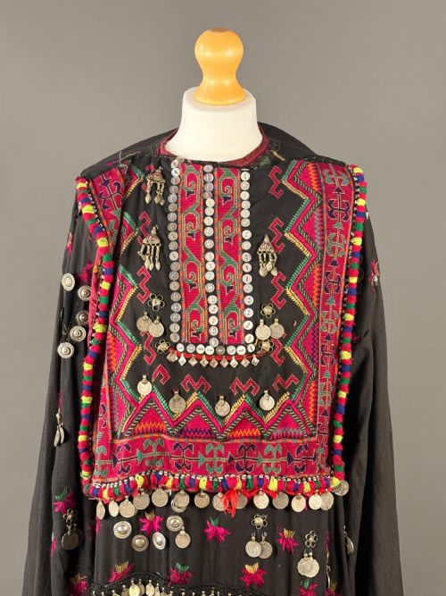 fig 1. An antique black Balochi ceremonial dress heavily adorned with colourful geometric silk embroidery, row upon row of hanging metal coins, and decorative buttons.