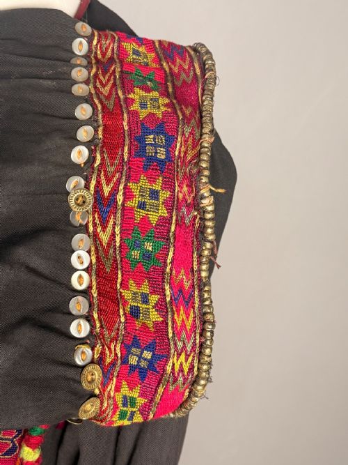 fig 2. An antique black Balochi ceremonial dress heavily adorned with colourful geometric silk embroidery, row upon row of hanging metal coins, and decorative buttons.