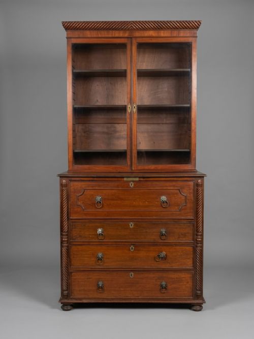 fig 1. A Regency mahogany secretaire bookcase featuring a glazed two-door cabinet, an open fall-front fitted writing drawer, and lower drawers flanked by rope-twist carved columns.