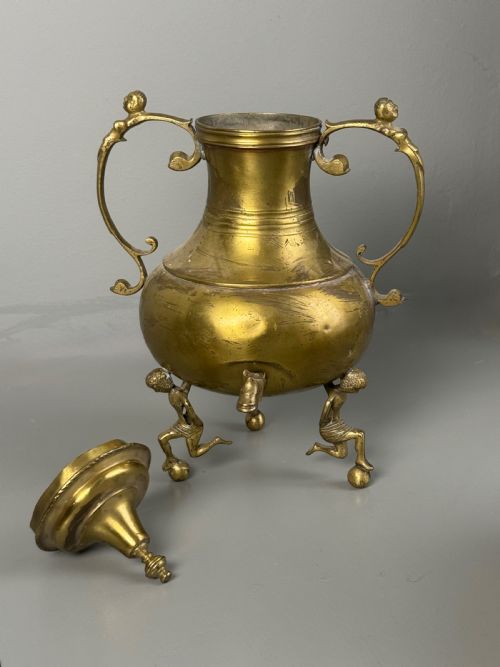 fig 2. An aged brass urn with caryatid supports and a top finial lid, displayed alongside a brass vessel featuring a raised dragon-form handle.