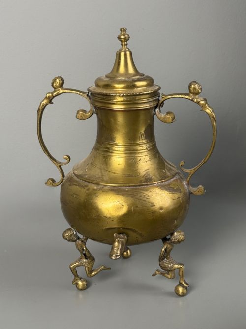 fig 3. An aged brass urn with caryatid supports and a top finial lid, displayed alongside a brass vessel featuring a raised dragon-form handle.