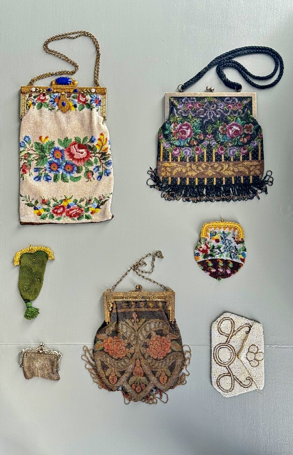 A collection of seven 1920s evening bags featuring micro-beaded floral patterns, silver mesh, and decorative metal frames arranged on a flat surface. View II