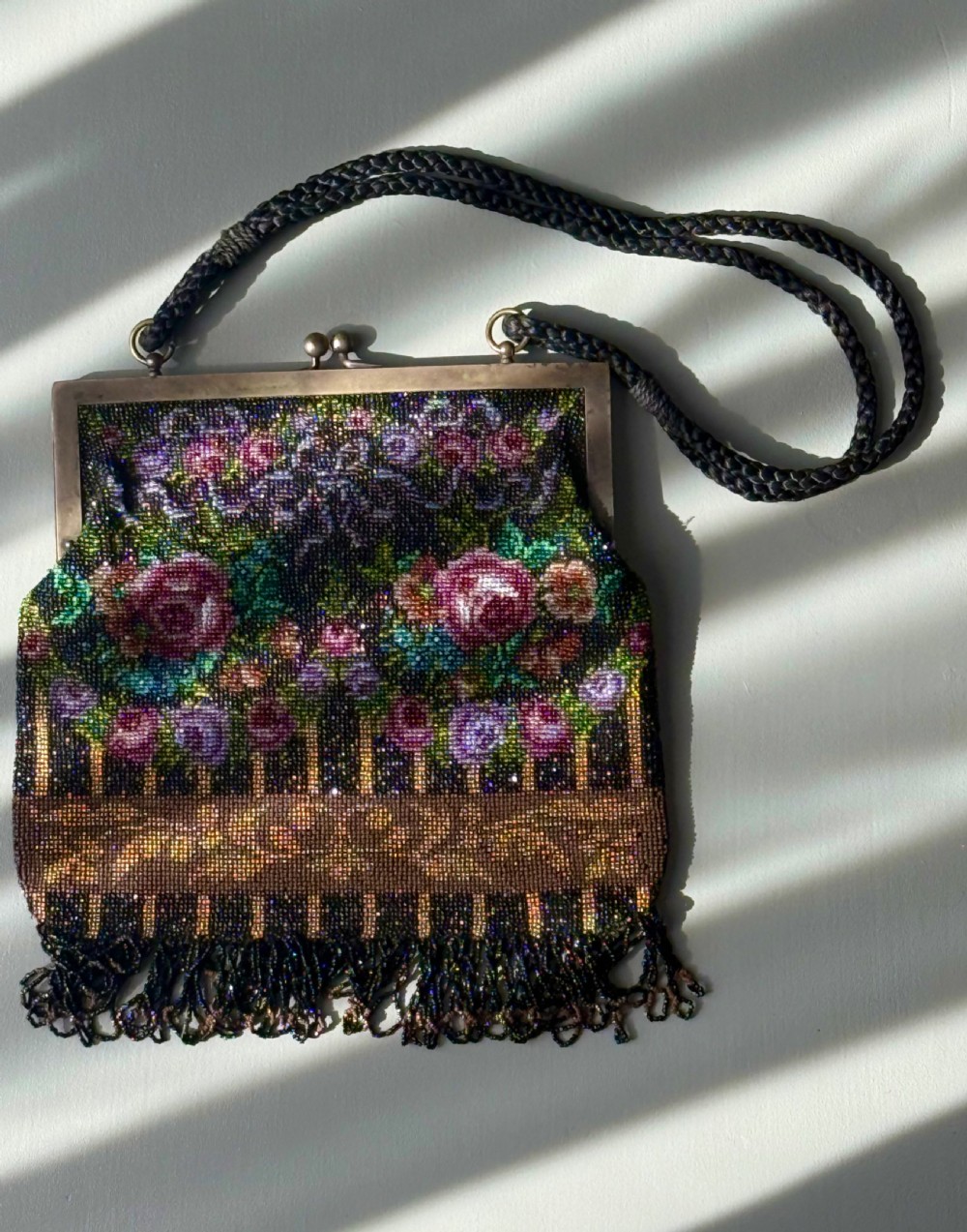 A collection of seven 1920s evening bags featuring micro-beaded floral patterns, silver mesh, and decorative metal frames arranged on a flat surface. View X