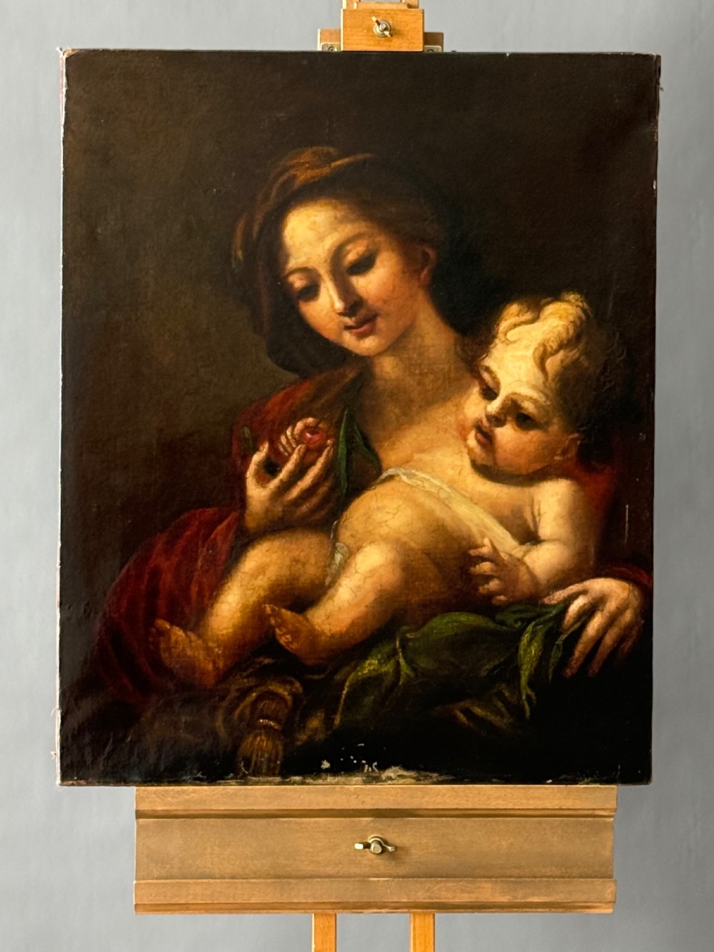 An early 18th-century Italian Baroque oil painting on canvas depicting the Madonna holding the infant Christ Child while holding cherries.