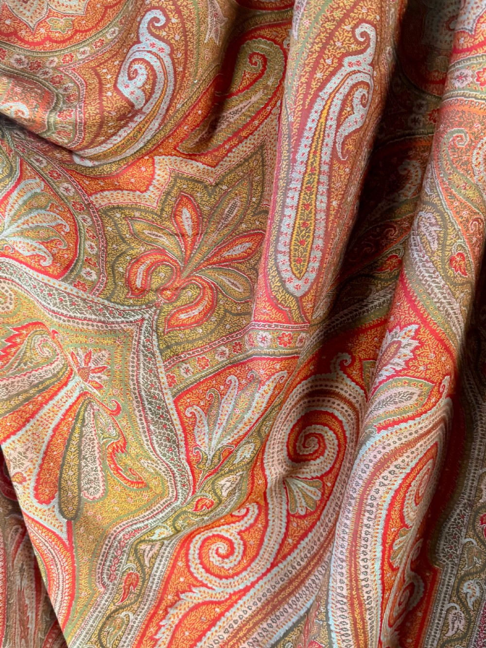 A large Victorian woven wool shawl featuring dense teardrop Paisley patterns in shades of terracotta, ochre, and green with a fringed border. View III