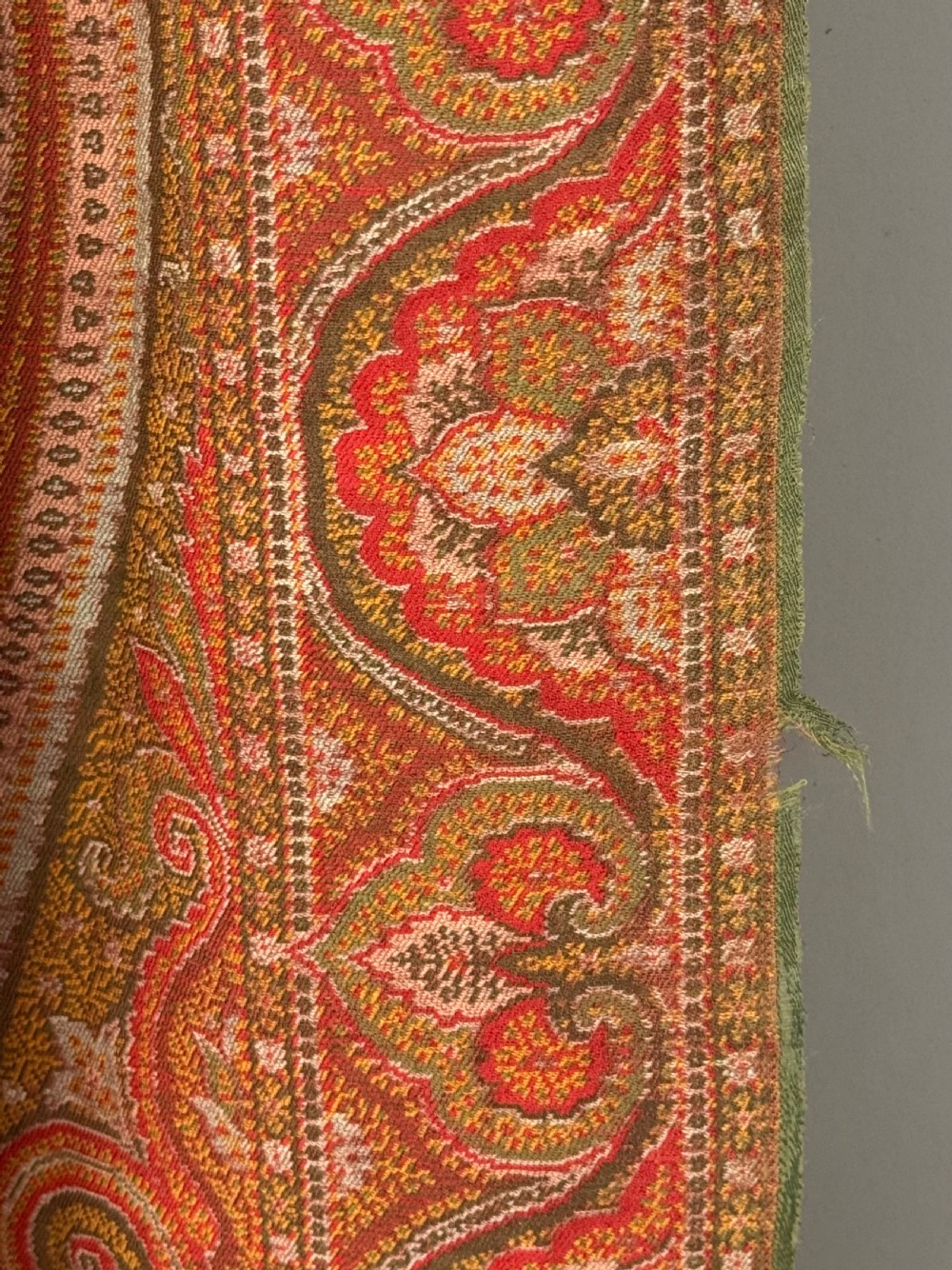 A large Victorian woven wool shawl featuring dense teardrop Paisley patterns in shades of terracotta, ochre, and green with a fringed border. View V