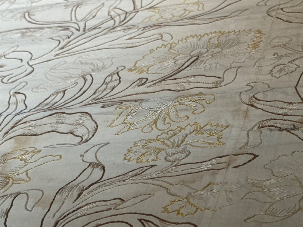 A cream-coloured Art Nouveau silk coverlet featuring hand-embroidered botanical motifs with a quilted border and pointed lace trim. View VIII