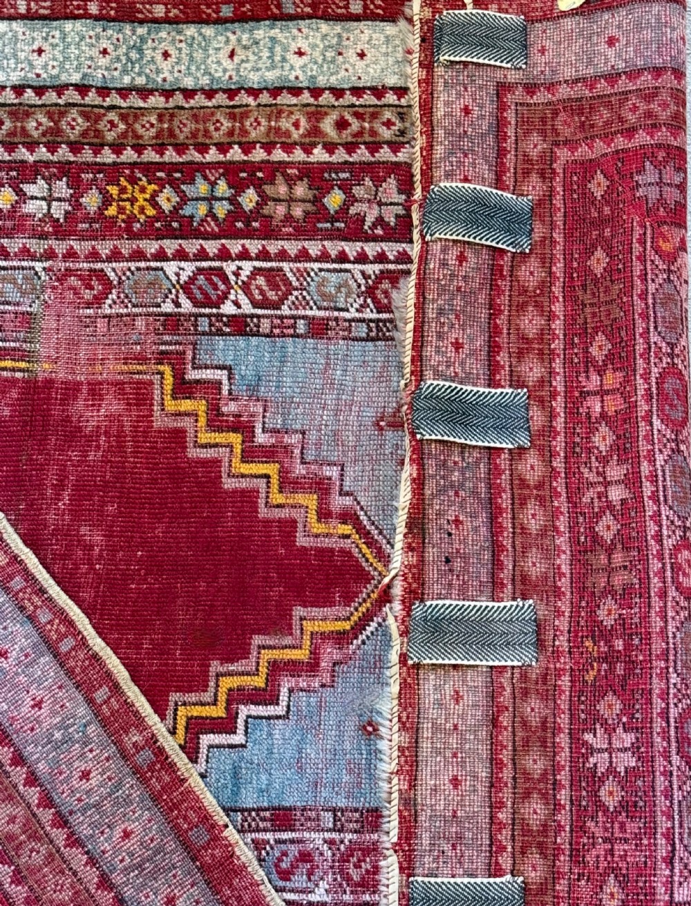 A late 19th-century Anatolian hand-knotted wool prayer rug featuring a central crimson mihrab niche motif surrounded by geometric borders in light blue, cream, and red. View V