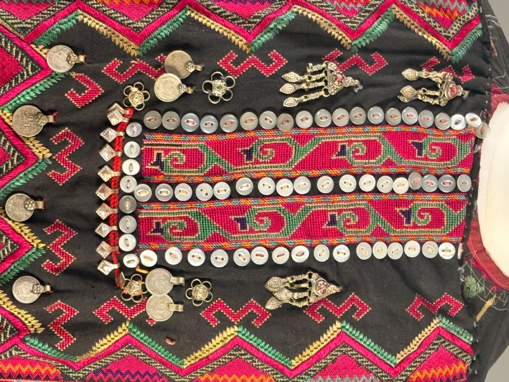 An antique black Balochi ceremonial dress heavily adorned with colourful geometric silk embroidery, row upon row of hanging metal coins, and decorative buttons. View V