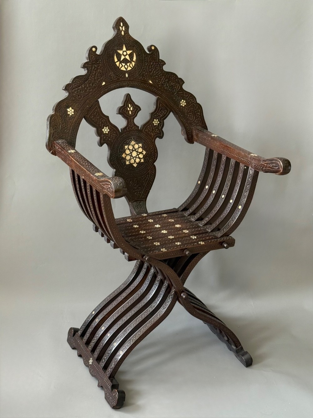 A 19th-century Ottoman dark hardwood X-frame armchair featuring detailed relief carvings and mother of pearl geometric inlays.