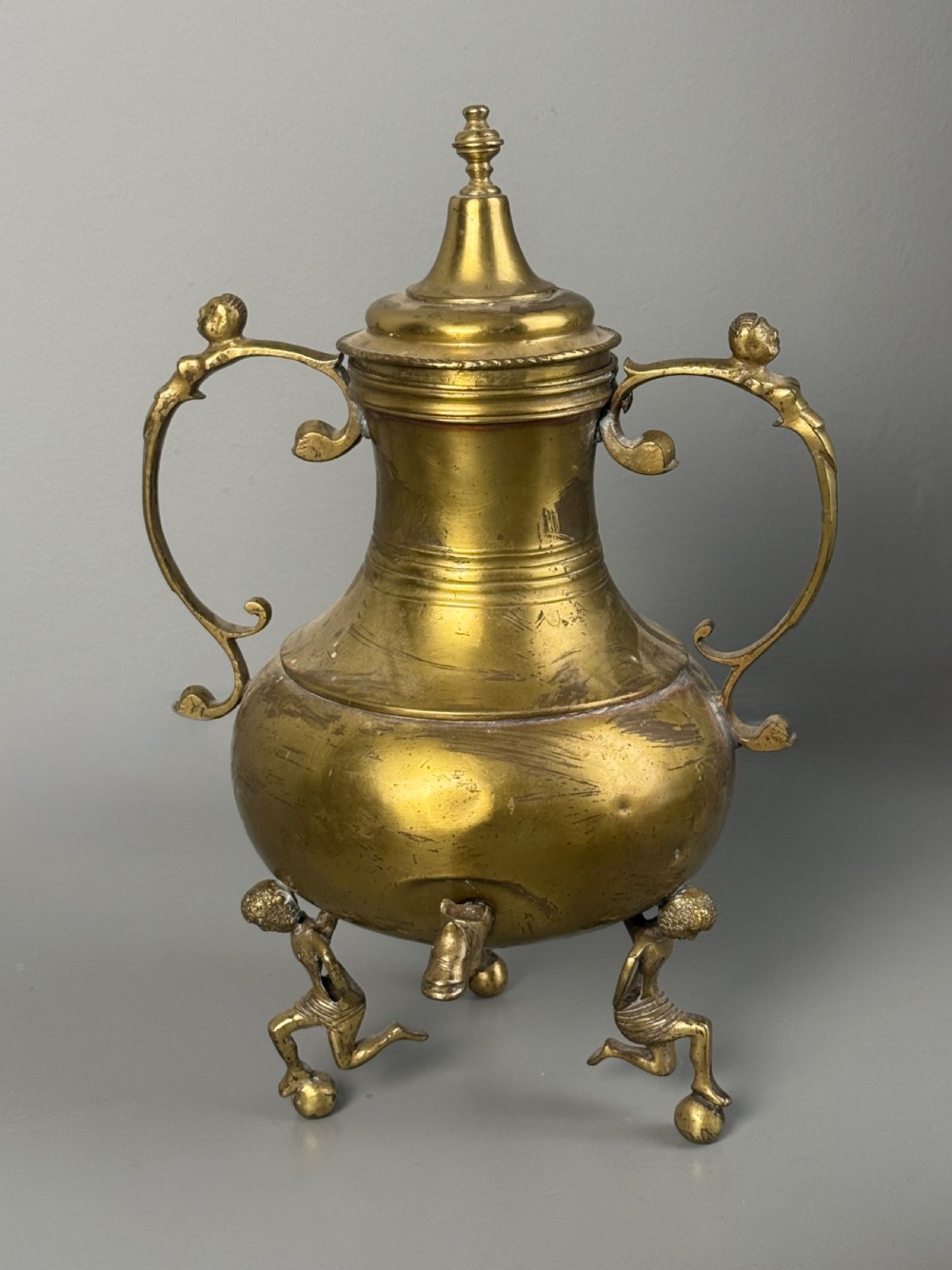 An aged brass urn with caryatid supports and a top finial lid, displayed alongside a brass vessel featuring a raised dragon-form handle. View IV