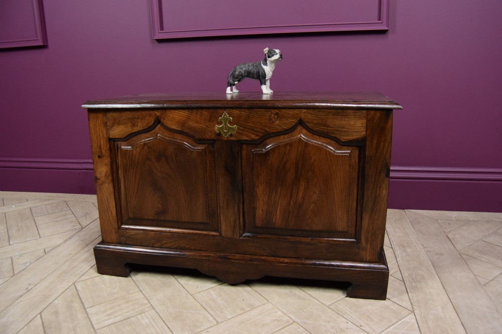 An early eighteenth-century dark oak Welsh coffer bach featuring two fielded arch panels, a brass escutcheon, and a shaped apron.