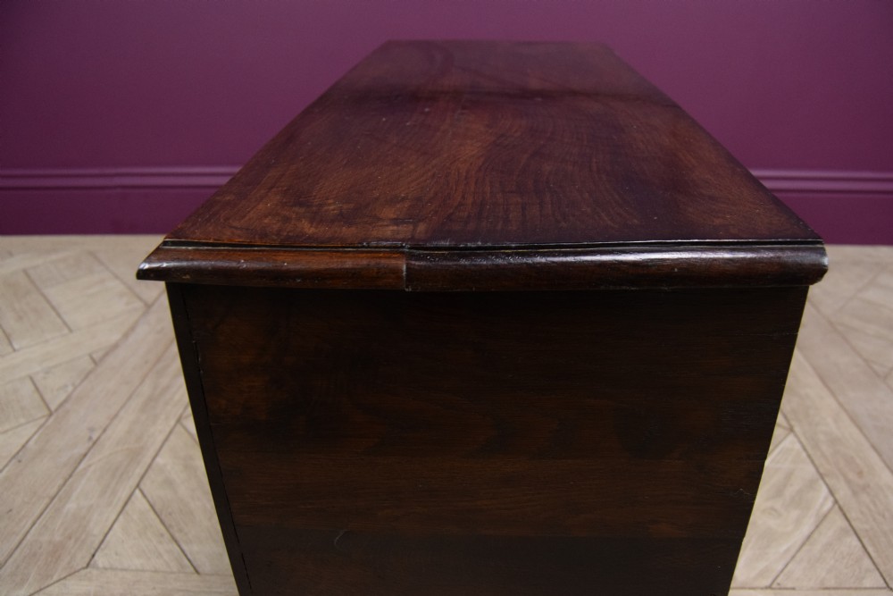 An early eighteenth-century dark oak Welsh coffer bach featuring two fielded arch panels, a brass escutcheon, and a shaped apron. View V