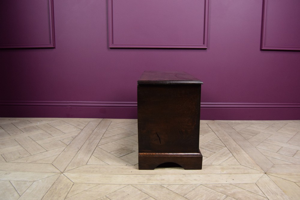 An early eighteenth-century dark oak Welsh coffer bach featuring two fielded arch panels, a brass escutcheon, and a shaped apron. View VII