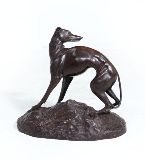 fig 1. A dark brown patinated bronze sculpture of a standing whippet dog on an uneven textured base.