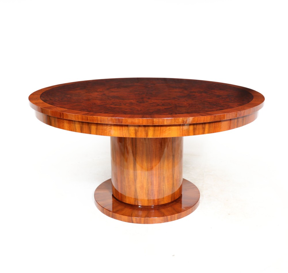 A circular Art Deco dining table featuring rich burr walnut veneer top with a central cylindrical pedestal base and round plinth.