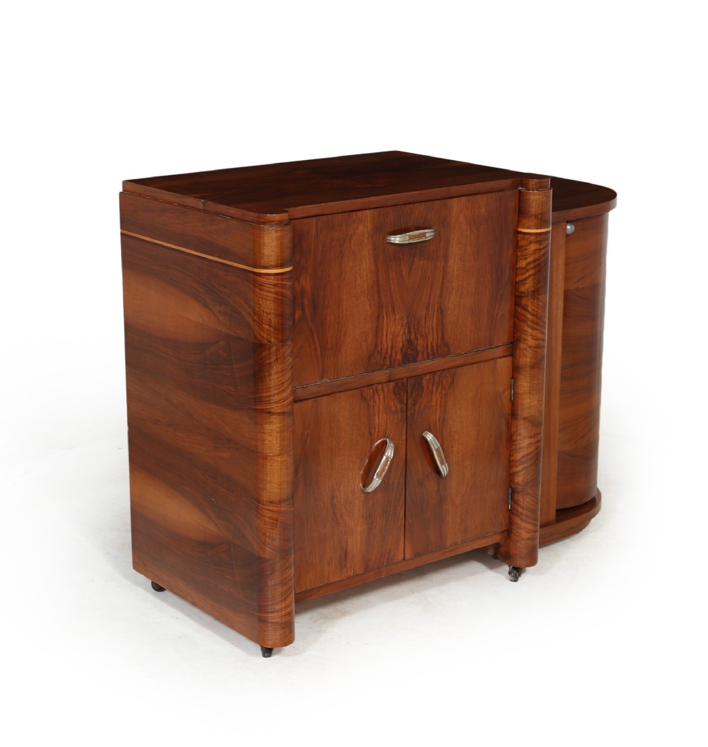 A French Art Deco cocktail cabinet featuring figured brown wood veneer, rounded corner columns, drop-front storage, and polished metal handles.