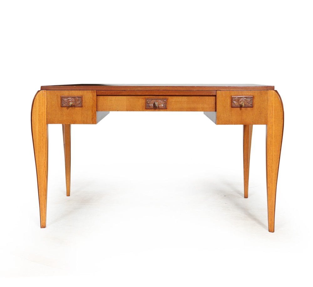 A French Art Deco oak writing desk featuring three frieze drawers with carved decorative handles and curved outer legs.