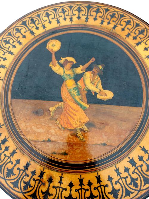 fig 1. A 19th-century circular Sorrento side table with detailed marquetry depicting dancing figures framed by a foliate border, set upon ebonised tripod legs.