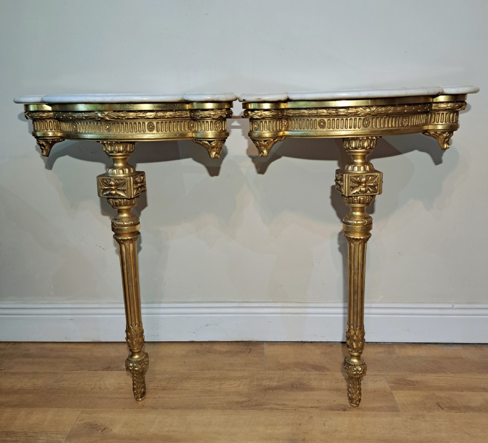 A pair of nineteenth-century French Neoclassical giltwood corner console tables with white marble tops and fluted single legs.
