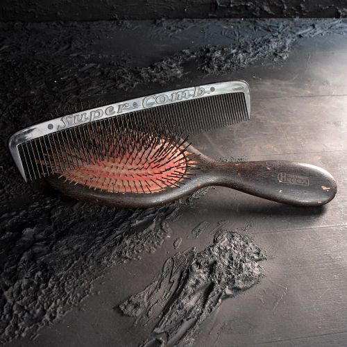 fig 1. A vintage dark wooden oval hairbrush with wire bristles resting alongside a large black comb embossed with the text Super Comb.