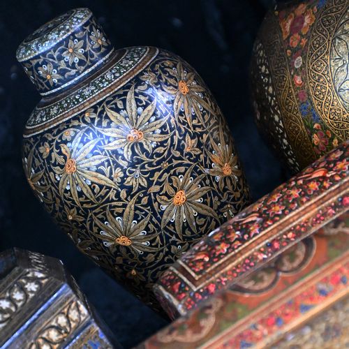 fig 1. A grouping of 19th-century Kashmiri papier-mache items featuring hand-painted lacquered boxes, canisters, and a bulbous urn in gold, black, and red floral designs.