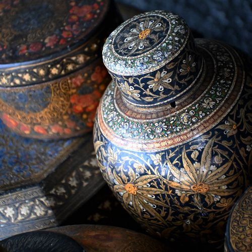 fig 3. A grouping of 19th-century Kashmiri papier-mache items featuring hand-painted lacquered boxes, canisters, and a bulbous urn in gold, black, and red floral designs.
