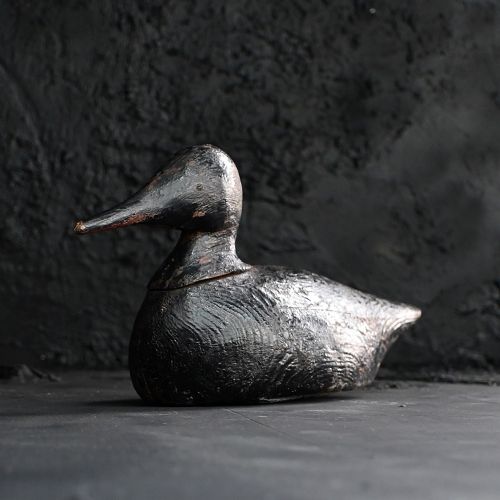 fig 2. A hand-carved wooden duck decoy featuring a distressed black paint finish and an elongated beak.