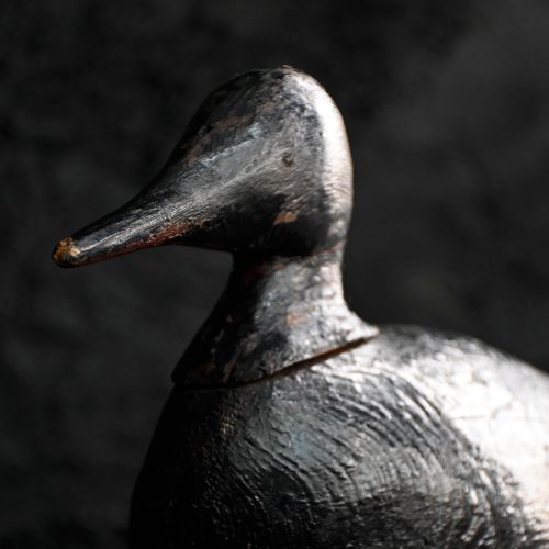 fig 3. A hand-carved wooden duck decoy featuring a distressed black paint finish and an elongated beak.