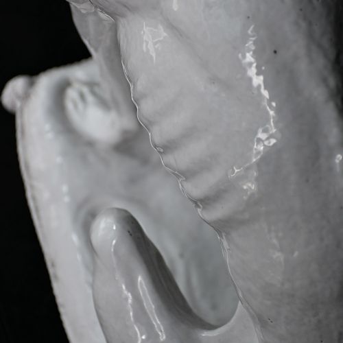 fig 2. A white glazed ceramic statue depicting a slender, seated greyhound dog resting on a tasselled cushion pedestal.