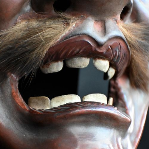 fig 1. A 19th-century carved wooden Japanese mask with a grimacing open mouth, exaggerated ears, applied hair details, and a dark lacquered finish.