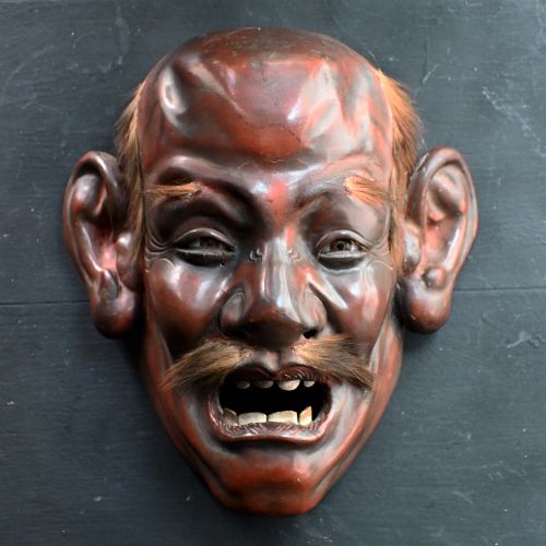 fig 2. A 19th-century carved wooden Japanese mask with a grimacing open mouth, exaggerated ears, applied hair details, and a dark lacquered finish.