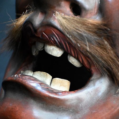 fig 4. A 19th-century carved wooden Japanese mask with a grimacing open mouth, exaggerated ears, applied hair details, and a dark lacquered finish.