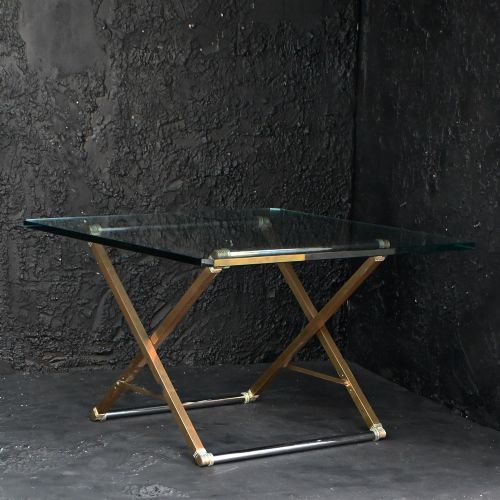 fig 1. A square clear glass side table supported by a brass and metal X-frame base.