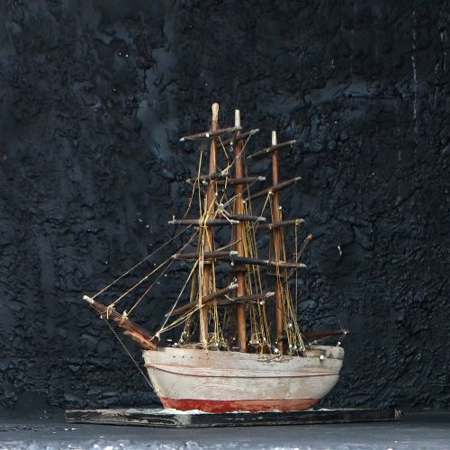 fig 3. An early 20th-century scratch-built wooden three-masted sailing ship model mounted on a textured green sea base inside a dark timber frame.